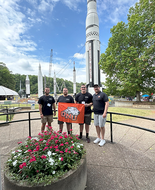 Photo of students with rockets in the background holding ONU flag