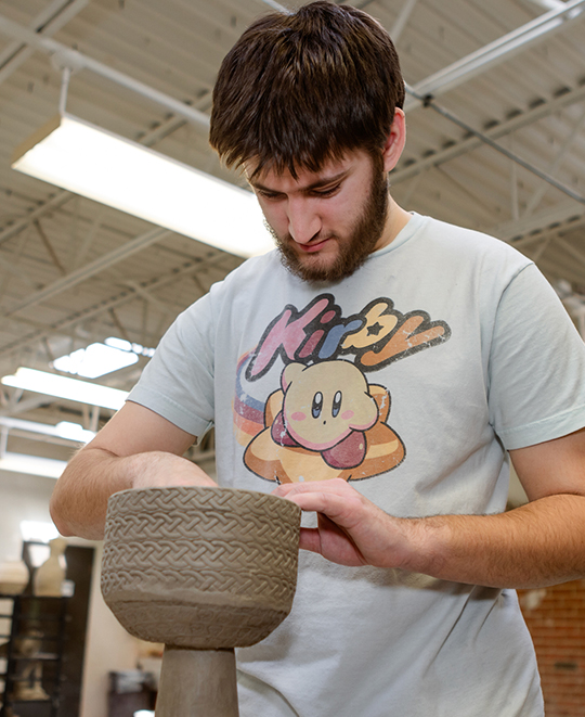 Photo of Art and Design class, ONU student working his clay vase-like structure