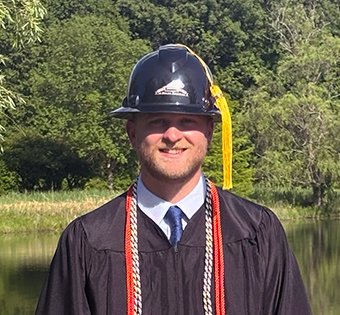 Photo of Andrew with his graduation robe and hard hat and tassel